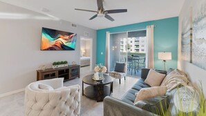 A spacious living room with a large painting, a ceiling fan, and a view of a balcony with outdoor furniture. - 3120-105 Resort Pool View Disney Universal Orlando (Kissimmee)