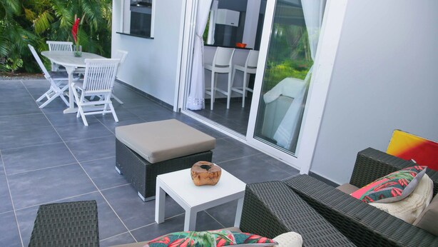 Une terrasse extérieure moderne, dotée d’un espace repas, de sièges et offrant une vue sur la verdure environnante.