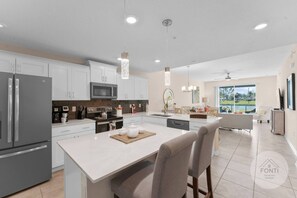 Una cocina moderna con gabinetes blancos, electrodomésticos de acero inoxidable y una isla central con asientos.