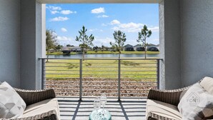 A balcony with wicker furniture, a glass table, and a view of a lake with houses in the background. - 3141-104 Resort Lake View Disney Universal Orlando (Kissimmee)
