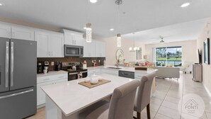 A modern kitchen with white cabinets, stainless steel appliances, and a central island with seating. - 3141-104 Resort Lake View Disney Universal Orlando (Kissimmee)