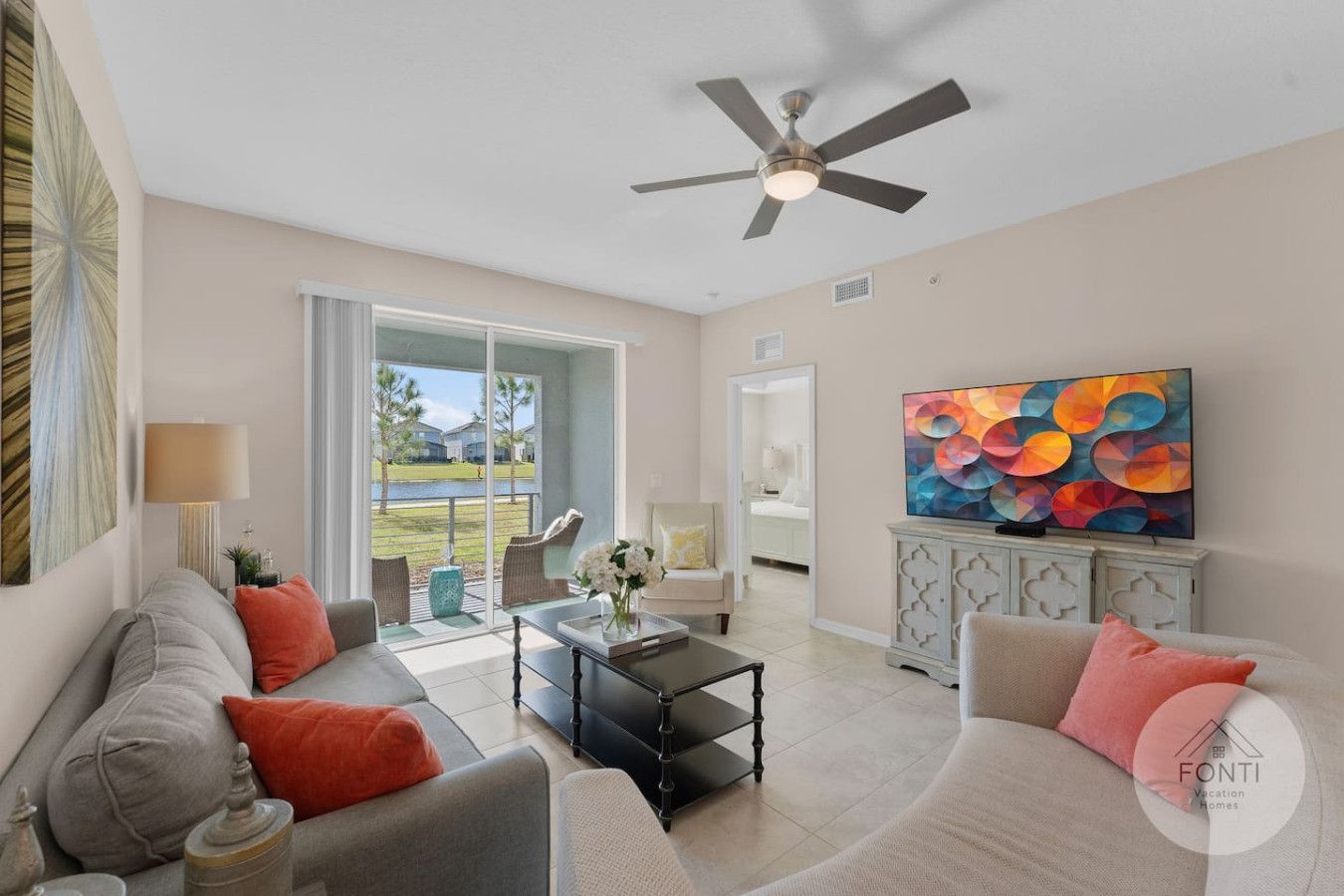 A spacious living room with a large window, a ceiling fan, and a colorful abstract painting on the wall.
