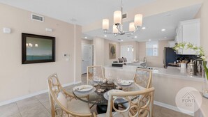 A modern kitchen with a central island, a dining area with a glass table, and a view of the ocean through a framed picture. - 3141-104 Resort Lake View Disney Universal Orlando (Kissimmee)