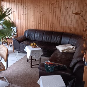 A living room with a dark leather sofa, a small table with a white tablecloth, a potted plant, and a lamp. - Ferienhaus in Brandenburg-ziesar (Ziesar)