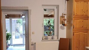 Une pièce avec une porte en bois donnant sur l’extérieur, une fenêtre avec vue sur la verdure, un radiateur et un meuble en bois.