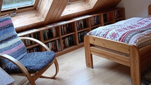 Une pièce avec un plafond en pente, des étagères en bois, un lit et une chaise.
