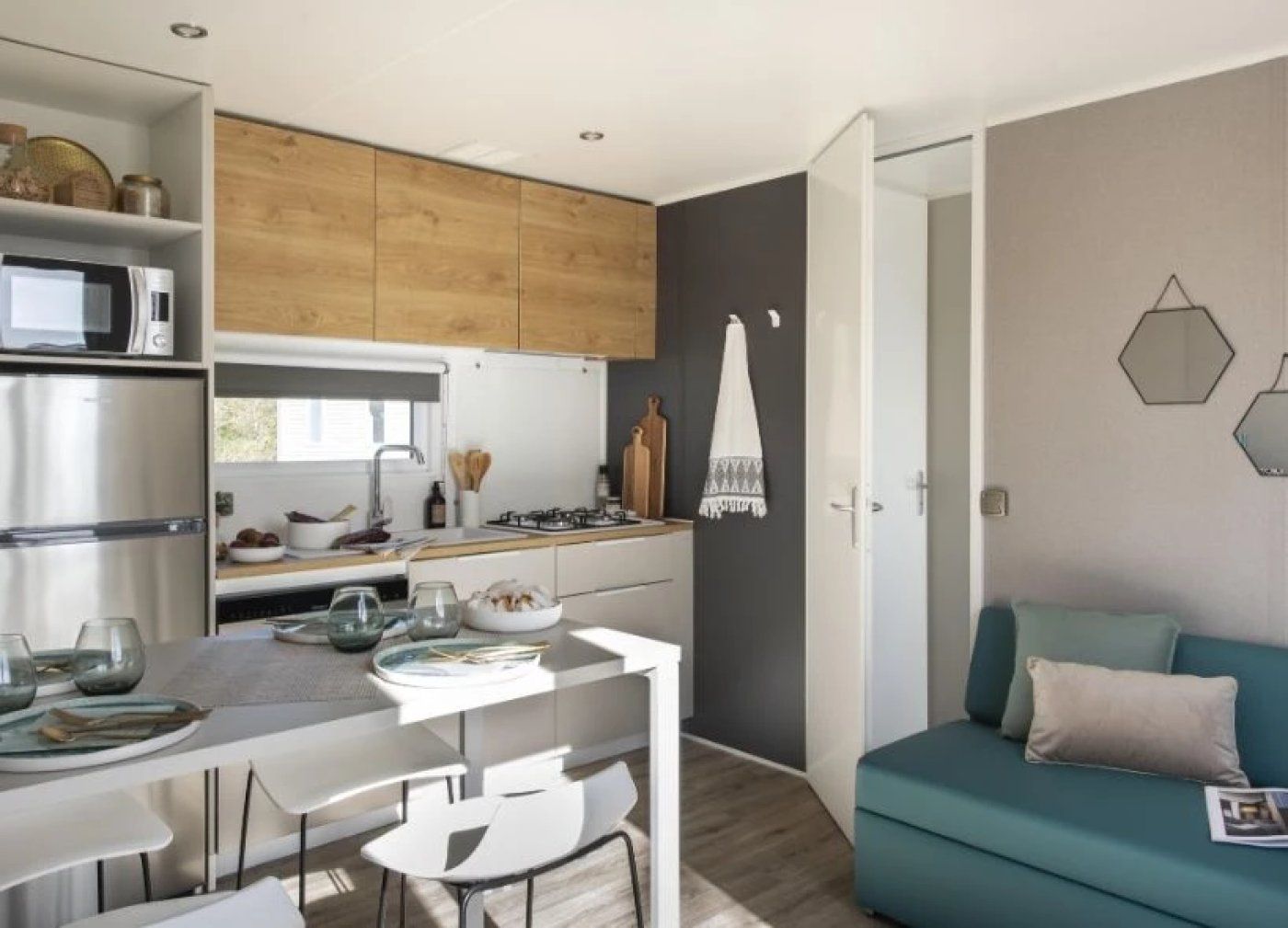 A compact kitchen with modern appliances, a dining area with chairs, and a teal sofa in a living space.