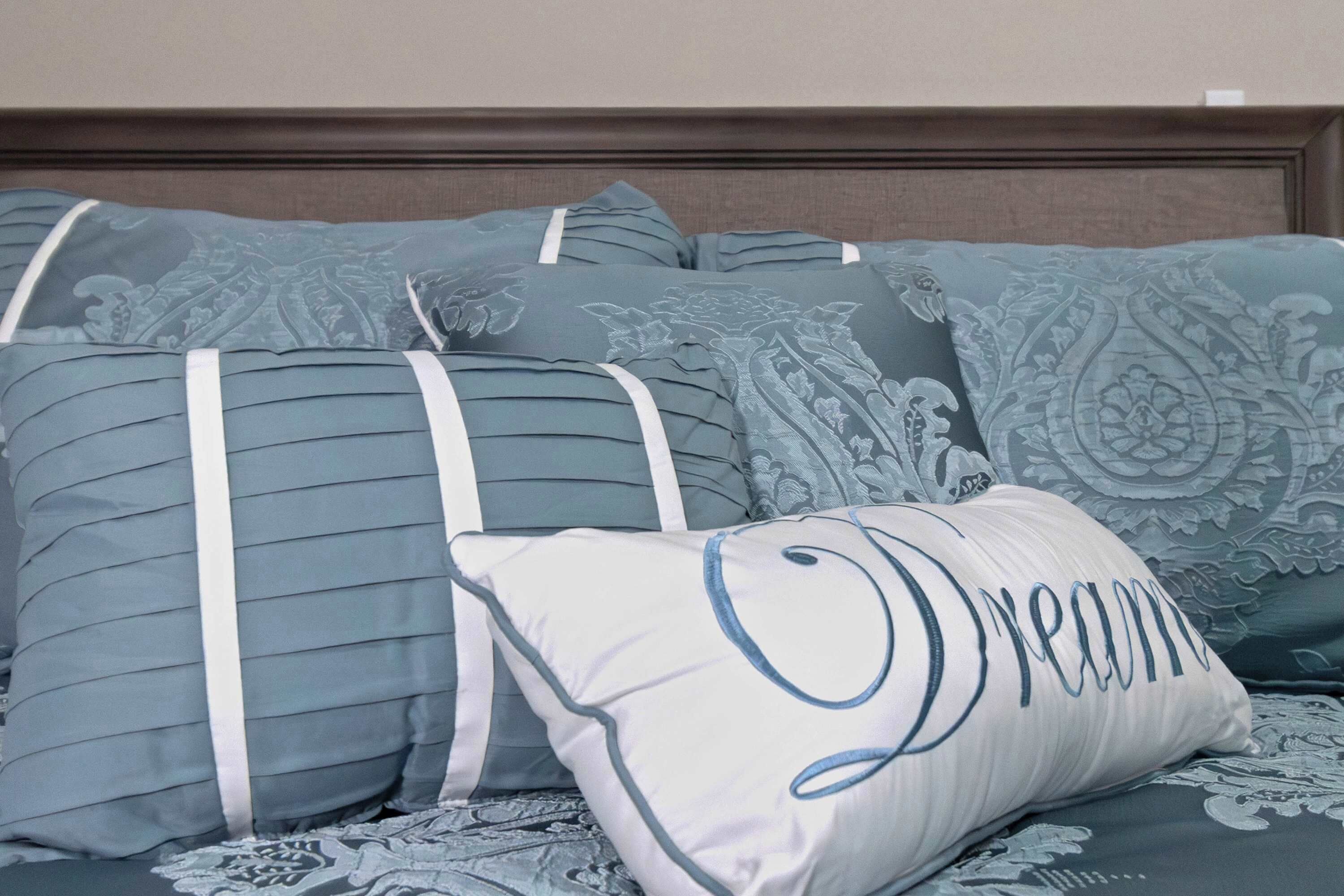 A bed with multiple pillows, one with the word 'Dream' embroidered on it.