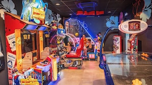 Un salón de juegos recreativos en el interior con diversas máquinas, incluyendo un juego de disparos y uno de carreras.