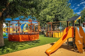 A playground with a slide, climbing structures, and a fenced play area. - ZEcamping parc aquatique animations locatif TV 23m2 6 pers (Le Château-d'Olonne)