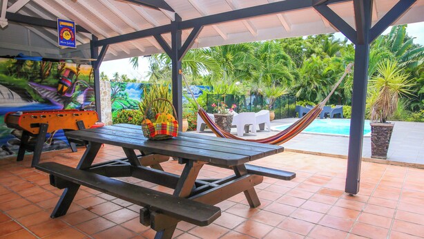 A covered patio area with a picnic table, a hammock, and a pool in the background.