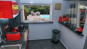 A compact kitchen with a window view of a pool, a red toaster, and a trash bin.