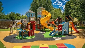 A playground with slides and climbing structures, surrounded by a fenced area and trees.