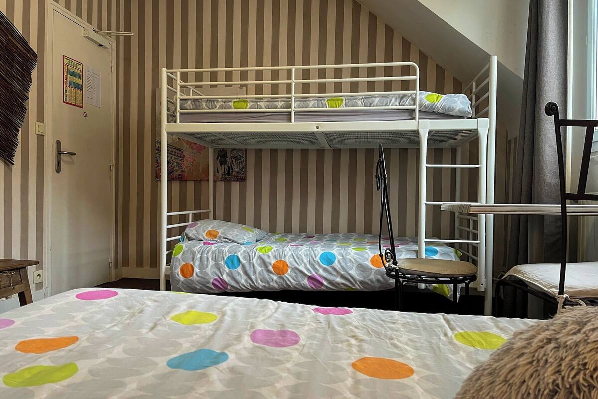 A bunk bed with a polka dot bedspread, a desk with a chair, and a window with curtains.