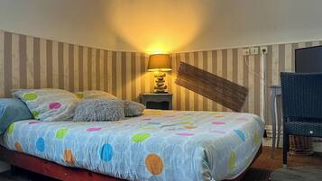 A bedroom with a bed, pillows, a lamp, a chair, and striped wallpaper.