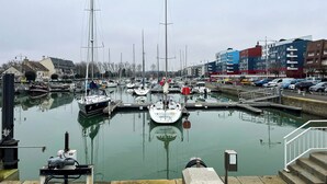 Ein Yachthafen mit mehreren vertäuten Booten, ein Gebäude mit der Beschriftung 'CAP HORN' und eine ruhige Wasseroberfläche, die die Umgebung spiegelt.