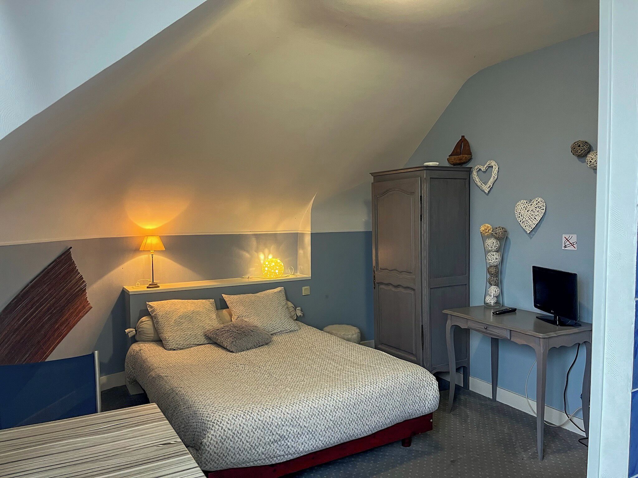 A bedroom with a sloped ceiling, a bed with a patterned bedspread, a desk with a computer, and decorative wall art.