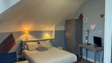 A bedroom with a sloped ceiling, a bed with a patterned bedspread, a desk with a computer, and decorative wall art.