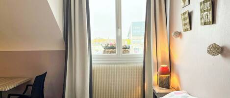A bedroom with a bed, a desk, a chair, a window with curtains, and wall decorations.