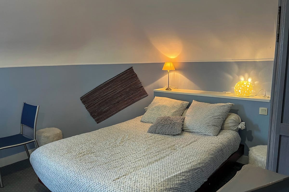 A bedroom with a bed, a chair, a wall-mounted lamp, and a decorative light fixture.
