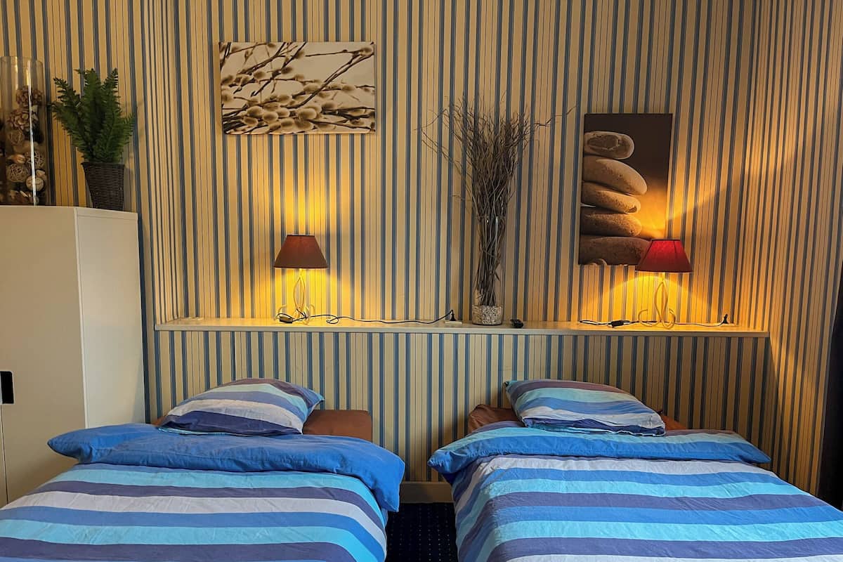 A hotel room with two beds, striped bedding, a wall-mounted shelf with decorative items, and two wall-mounted lamps.