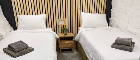 A room with two single beds, a small bedside table with a lamp, and a wooden slat headboard.
