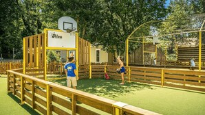 A basketball court with a yellow fence, a basketball hoop, and a netted play area.