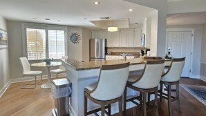 A modern kitchen with a central island, white cabinetry, and a dining area with bar stools. - 3rd Floor Villa w/ Ocean Views & Amenities (Hilton Head Island)