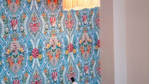 Une pièce avec un papier peint à motifs, un lit avec des oreillers blancs et une lampe suspendue.