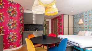 Une chambre moderne avec une table ronde, des chaises colorées, un lit et un coin cuisine.