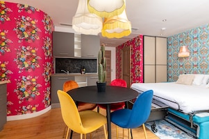 A modern room with a round table, colorful chairs, a bed, and a kitchen area.