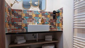 Une salle de bain avec un lavabo, trois miroirs, un porte-serviettes et un mur recouvert de carreaux décoratifs.