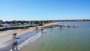 Une zone côtière avec une plage de sable, une jetée qui s’avance dans l’eau et, au loin, des immeubles résidentiels.