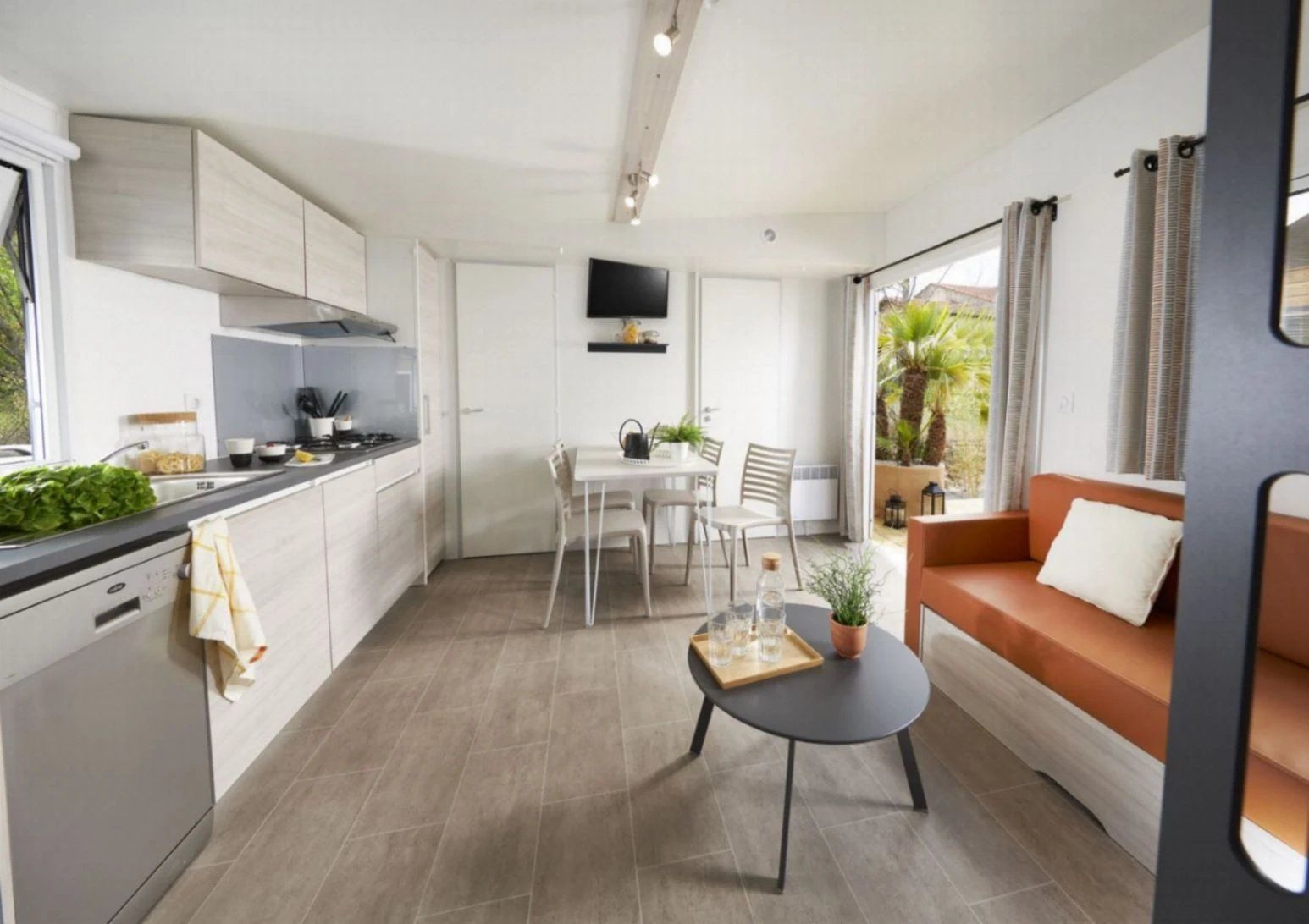 Een moderne keuken met witte kasten, een eethoek met een tafel en stoelen, en een zithoek met een bank en salontafel.