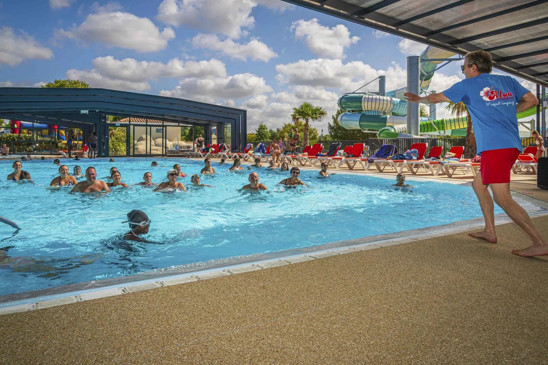 A swimming pool with people in the water, a covered area, and a person standing on the poolside.