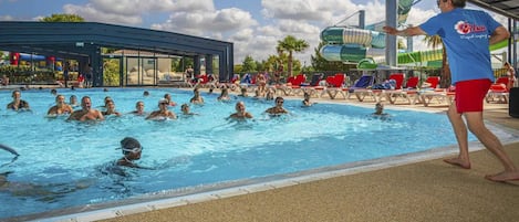 A swimming pool with people in the water, a covered area, and a person standing on the poolside.