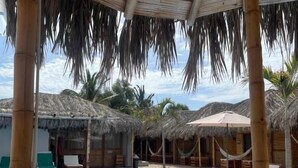Un área de piscina con techo de paja, sillas de descanso y una piscina azul cristalina.