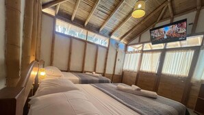 Habitación con dos camas, paredes de madera, un televisor en la pared y un ventilador de techo.