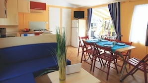 A compact kitchen with a dining area, a blue sofa, and a laptop on a table. - ZEcamping animations espace aquatique piscine couverte et restaurant (Saint-Hilaire-de-Riez)