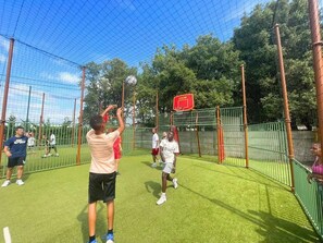 Een binnensportzaal met een basketbalveld, omgeven door een net en met bomen op de achtergrond.
