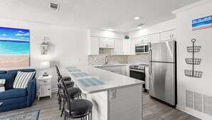 A modern kitchen with white cabinetry, a stainless steel refrigerator, and a central island with bar stools.
