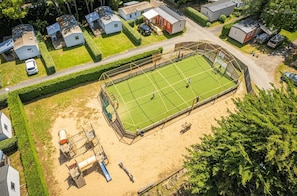 An aerial view of a residential area with a tennis court, houses, and a sandy area with equipment. - ZEcamping espace aquatique pet friendly club enfant mobil-home TV clim (Saint-Hilaire-de-Riez)