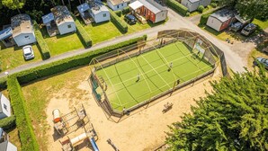 An aerial view of a residential area with a tennis court, houses, and a sandy area with equipment. - ZEcamping parc aquatique dog friendly animations locatif TV 28m2 (Saint-Hilaire-de-Riez)
