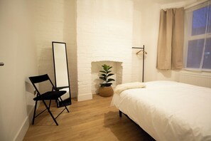 A bedroom with a bed, a chair, a mirror, a potted plant, and a window with curtains.