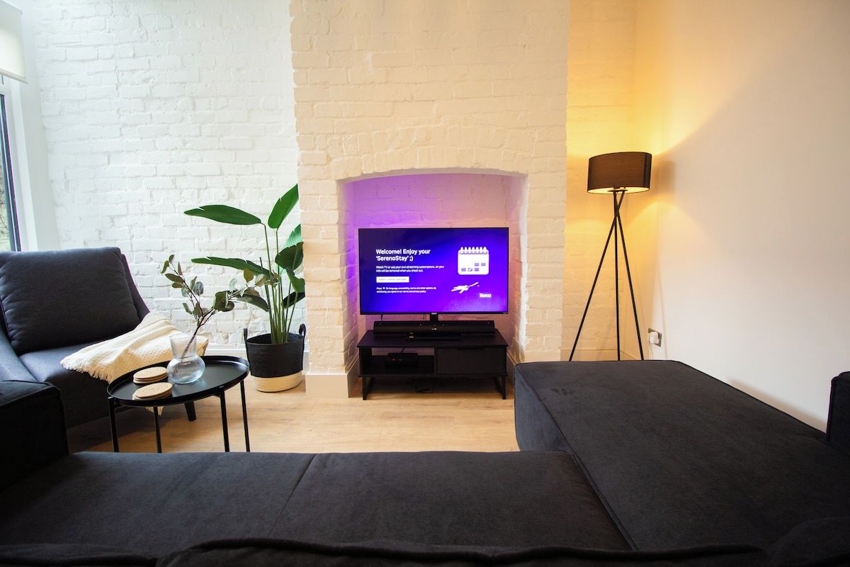 A modern living room with a flat-screen TV, a sofa, a coffee table, a potted plant, and a floor lamp.