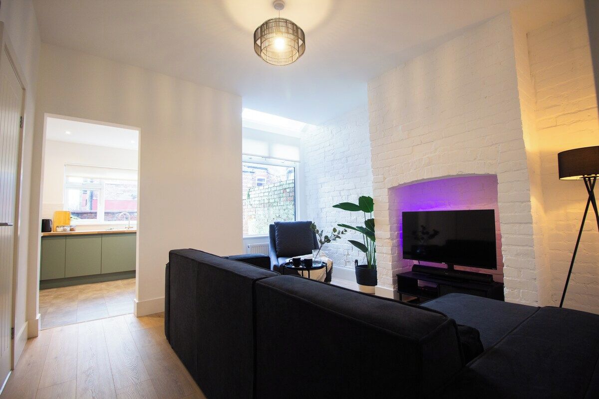 Un salon moderne avec un canapé noir, un téléviseur à écran plat et une plante en pot.