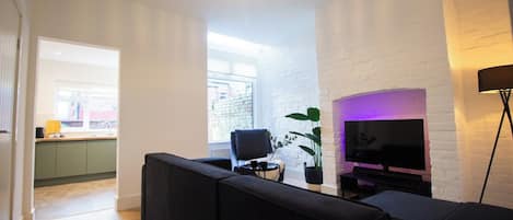 Una sala de estar moderna con un sofá negro, un televisor de pantalla plana y una planta en maceta.