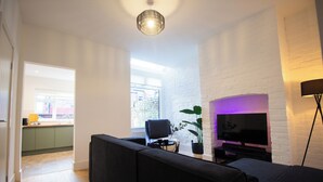A modern living room with a black sofa, a flat-screen TV, and a potted plant. - Comfy 4 Bed, Quiet Stay, Near the City Center, Free Parking & Speedy WIFI  (Manchester)