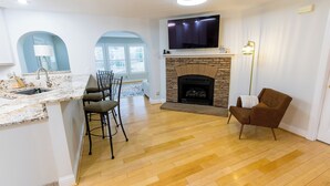 A modern kitchen with a marble countertop, a dining area with chairs, a fireplace, and a TV mounted above it.