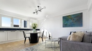 Une cuisine moderne avec des meubles blancs, un coin repas doté d’une table ronde et un canapé gris dans un espace de vie lumineux.